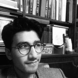 Black and white photograph of Gianamar Giovannetti-Singh in front of a bookshelf